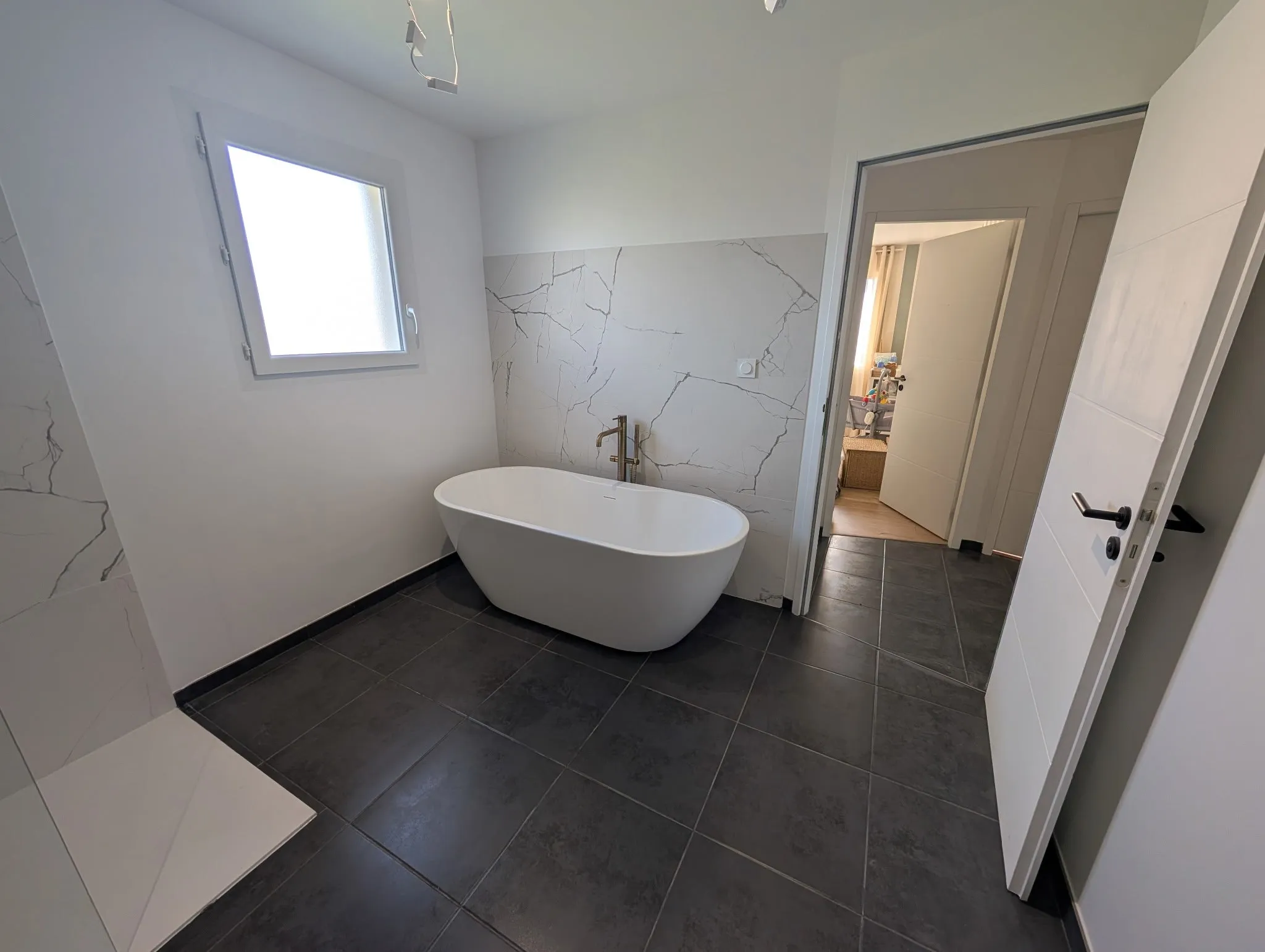 Salle de bains rénovée à Moulins : baignoire îlot, faïence effet marbre et carrelage gris foncé
