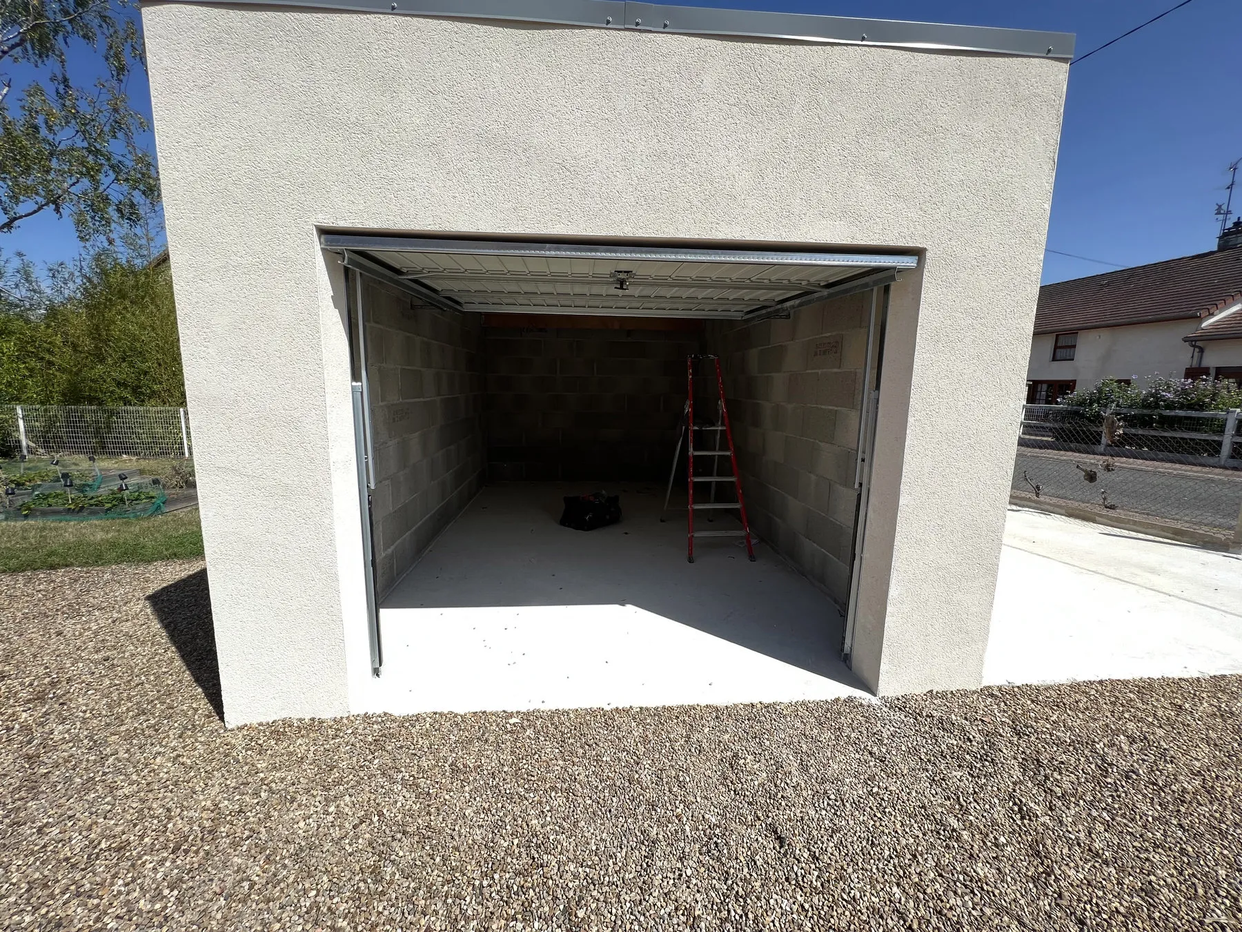 Garage indépendant à toit plat, enduit clair et porte sectionnelle noire, à Sermoise-sur-Loire
