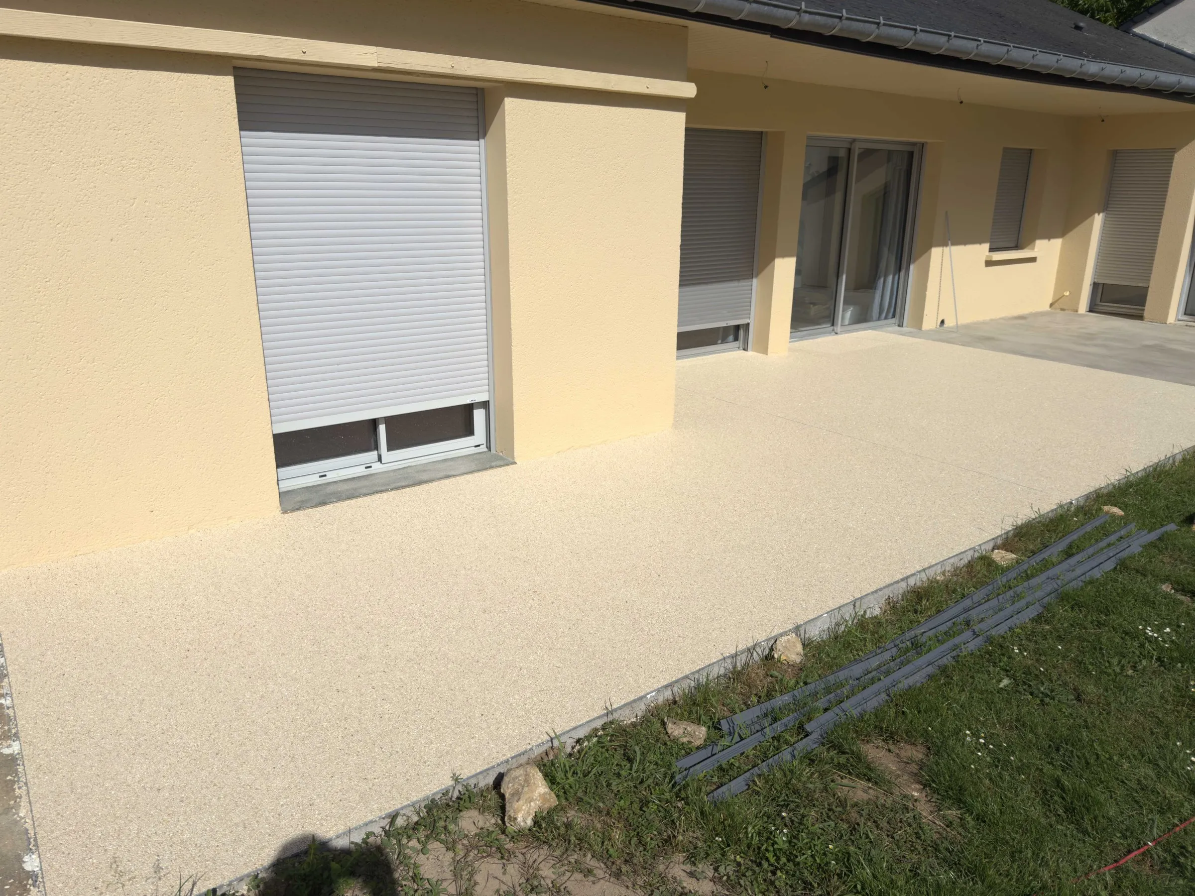 Terrasse en résine drainante claire posée le long d’une maison