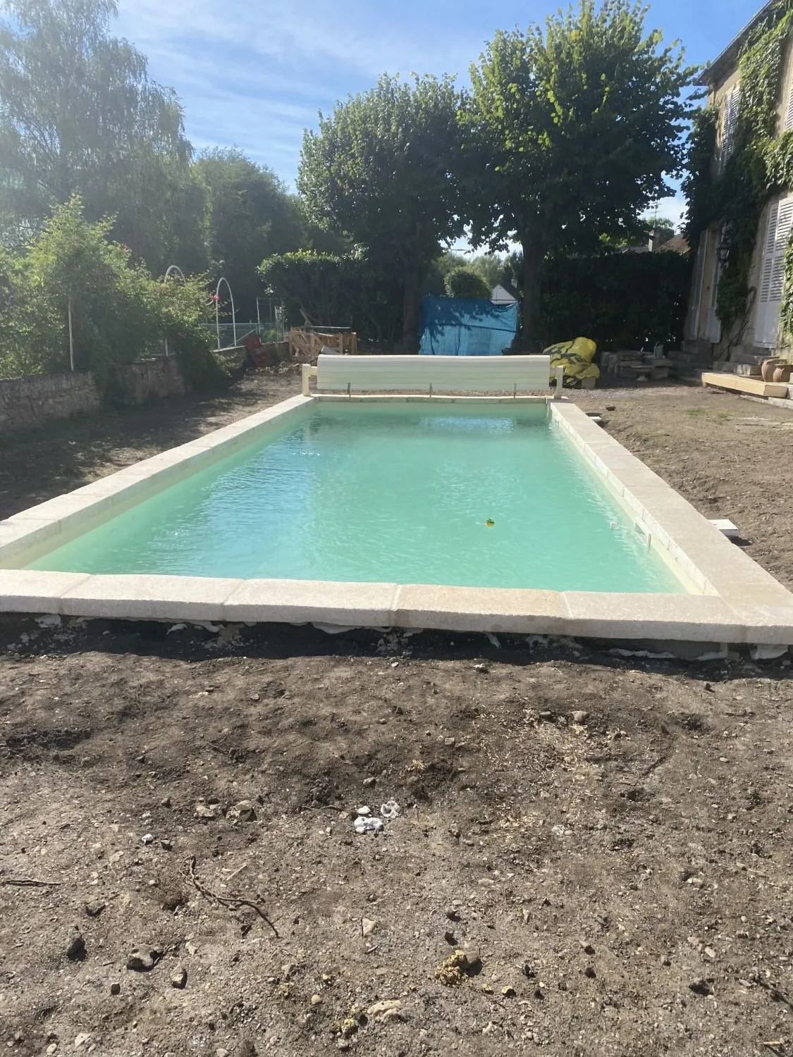 Piscine terminée et en eau dans un jardin de la Nièvre, margelles claires et volet roulant