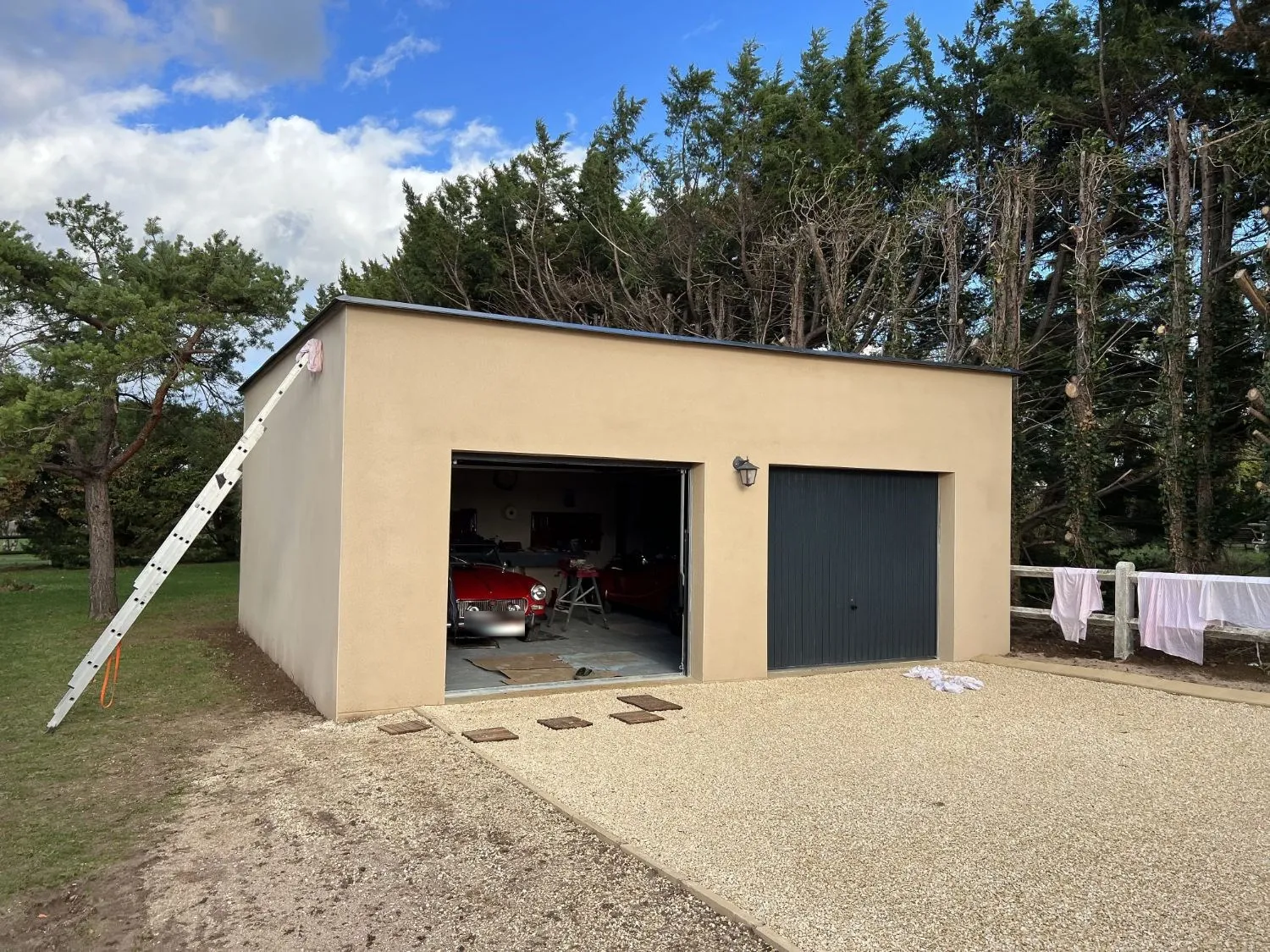 Garage double terminé à Magny-Cours : enduit beige, toit plat, deux portes basculantes et allée gravillonnée