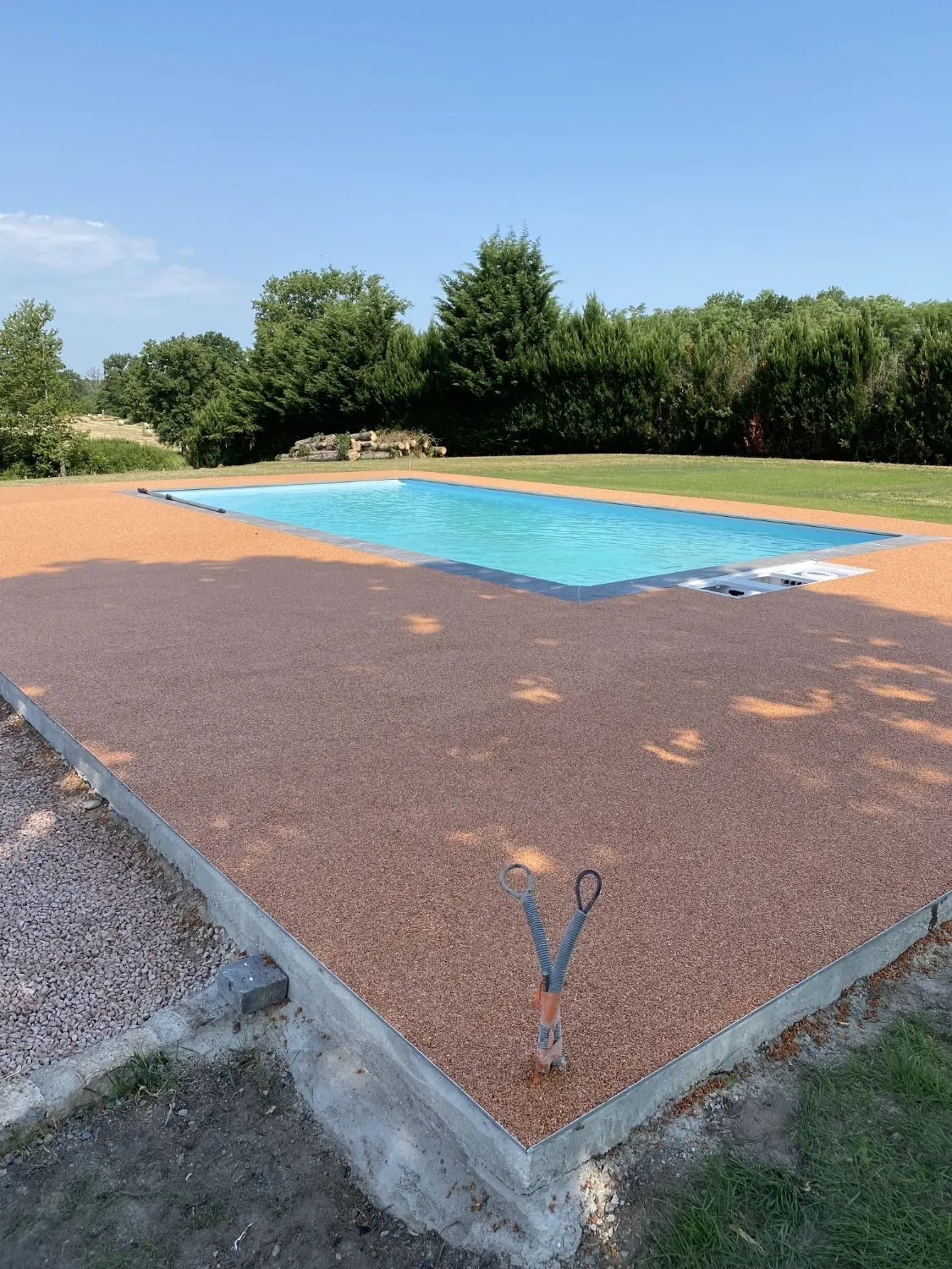 Plage de piscine en résine drainante couleur terre cuite, bordée d’un profilé