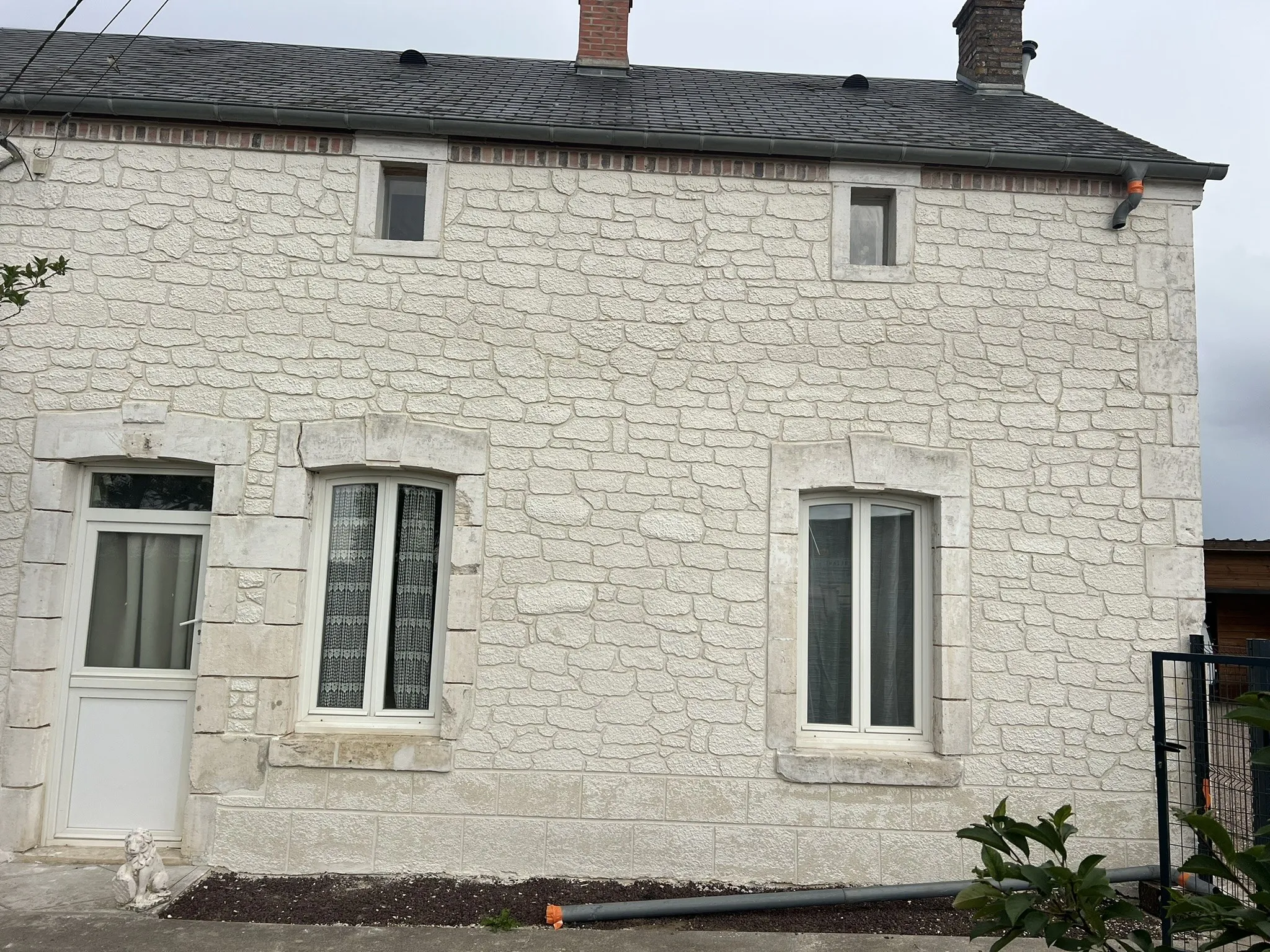 Façade de maison en enduit imitation pierre, encadrements de fenêtres soulignés