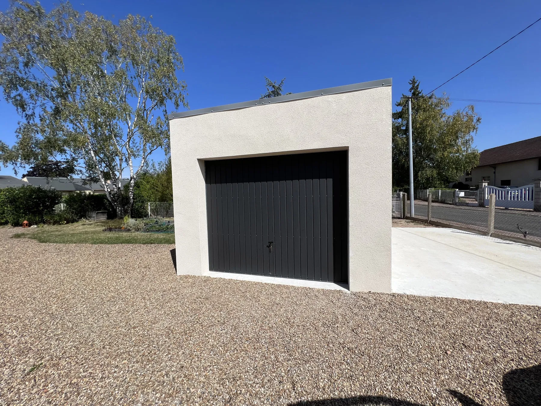 Garage à toit plat enduit avec porte sectionnelle noire